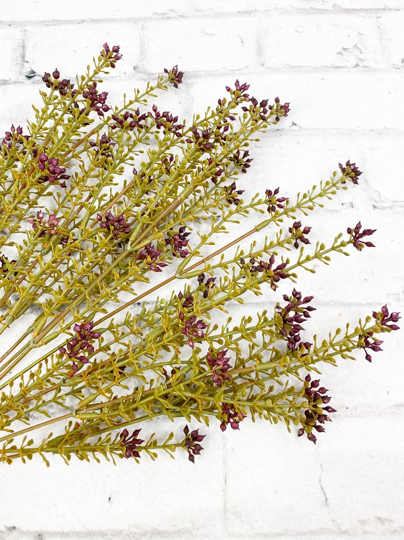 May include: A bunch of artificial greenery with small purple flowers. The stems are green and the leaves are a light green color.