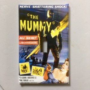 May include: A decorative light switch cover featuring a vintage movie poster design for "The Mummy." The poster art includes a mummy figure, a terrified woman, and the text "NERVE-SHATTERING SHOCK!" in a glossy finish.
