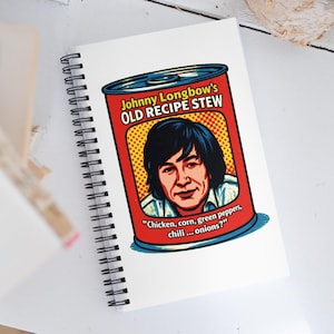 May include: A spiral-bound notebook featuring a retro-style design of a stew can. The can is red with a yellow dotted background and a portrait of a man. Text reads "Johnny Longbow's OLD RECIPE STEW".