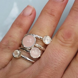 May include: A set of four silver rings with pink and white gemstones. The rings are stacked on a finger.