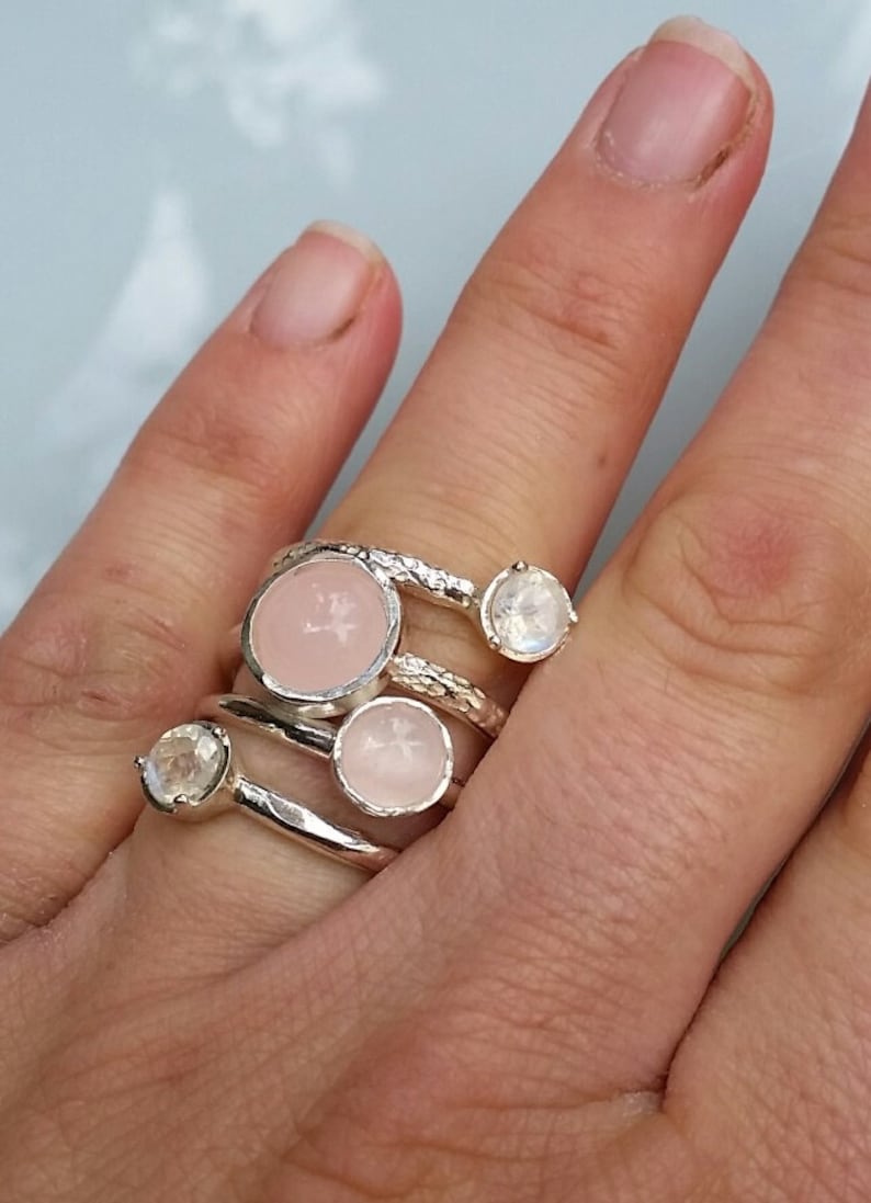 May include: A set of four silver rings with pink and white gemstones. The rings are stacked on a finger.