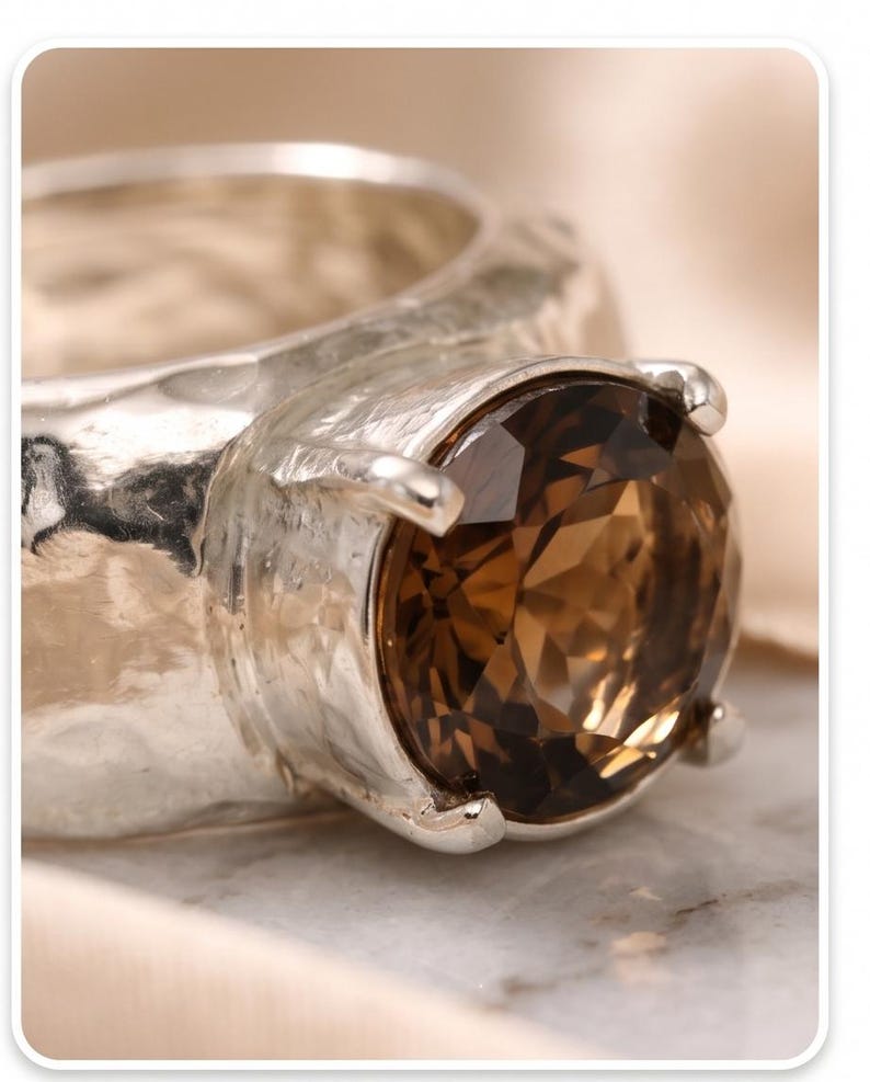 May include: A silver ring with a large, round, brown gemstone. The ring has a textured band and four prongs holding the stone. The gemstone is faceted, catching the light and displaying various shades of brown.