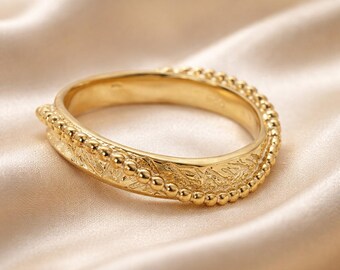 May include: A gold ring featuring a central band with a textured, organic surface pattern. The ring is bordered on both sides by a delicate row of small, uniform gold beads that create a beaded edge along the entire circumference of the band.