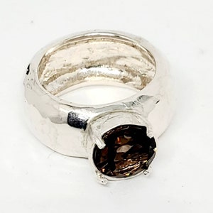 May include: A silver ring with a large, round, brown gemstone. The ring has a thick band with a textured surface. The gemstone is held in place by four prongs.