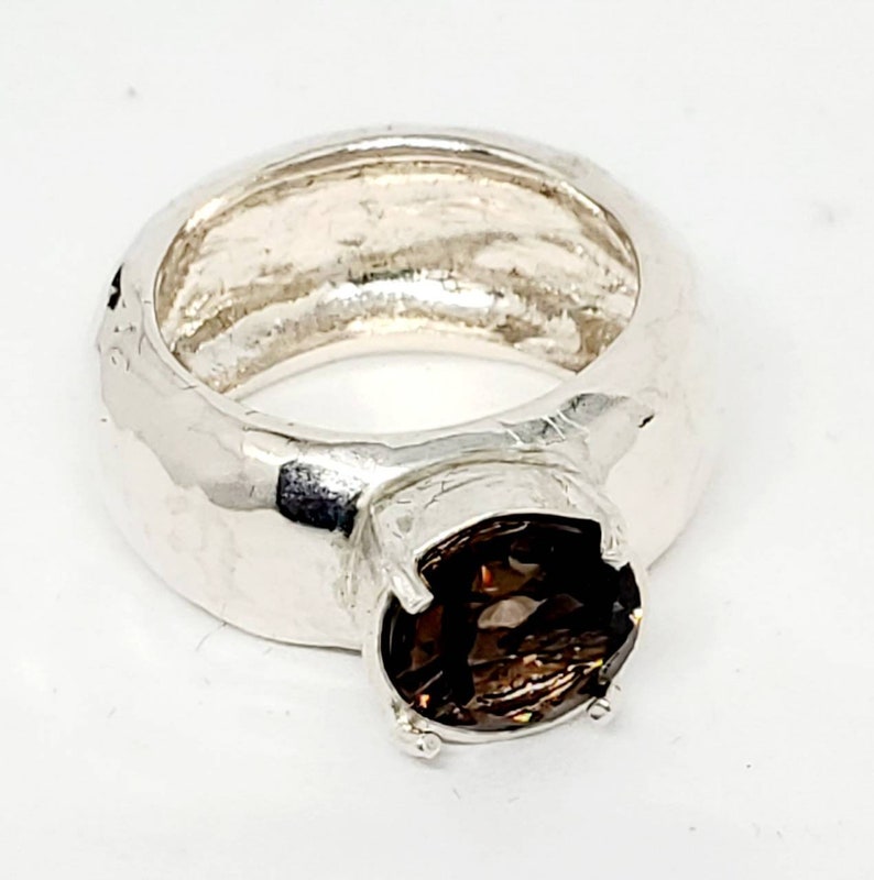 May include: A silver ring with a large, round, brown gemstone. The ring has a thick band with a textured surface. The gemstone is held in place by four prongs.