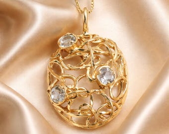 Può includere: Una collana con pendente color oro caratterizzata da un design ovale traforato composto da fili di metallo intrecciati. Tre pietre trasparenti a taglio rotondo sono incastonate nell'intricata struttura metallica dorata, sospesa a una catena abbinata.