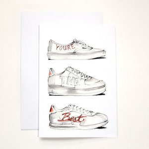 May include: A white card with a black and white illustration of three trainers. The trainers have the words "You're the Best" written on them in red.