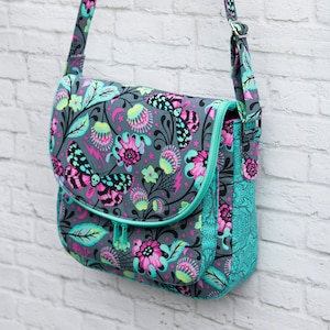 Può includere: Borsa a tracolla grigia con un colorato motivo floreale e a farfalle. La borsa presenta una cerniera, finiture e pannello laterale turchese. La tracolla regolabile e la patta aggiungono funzionalità a questo accessorio.