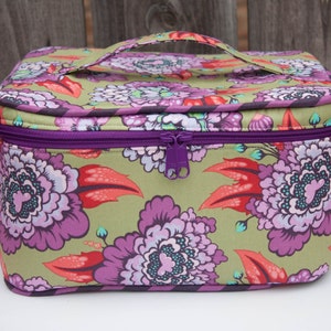 May include: A floral print cosmetic bag with a purple zipper and handle. The bag features a repeating pattern of large purple and pink flowers with red leaves on a light green background. The zipper and handle are a matching purple color.