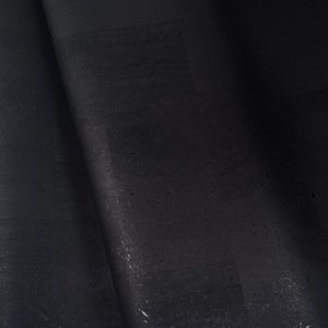 Pode incluir: Close-up de um rolo de material de cortiça preta. A cortiça tem uma superfície texturizada com variações sutis de tom e pequenas manchas de cor clara. O material está parcialmente enrolado, revelando sua espessura e flexibilidade.