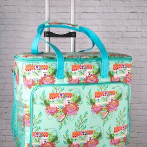 May include: A rolling sewing machine tote bag with a teal floral pattern featuring sewing machines and flowers. The bag has teal handles and trim, a mesh side pocket, and a telescoping handle for easy transport.