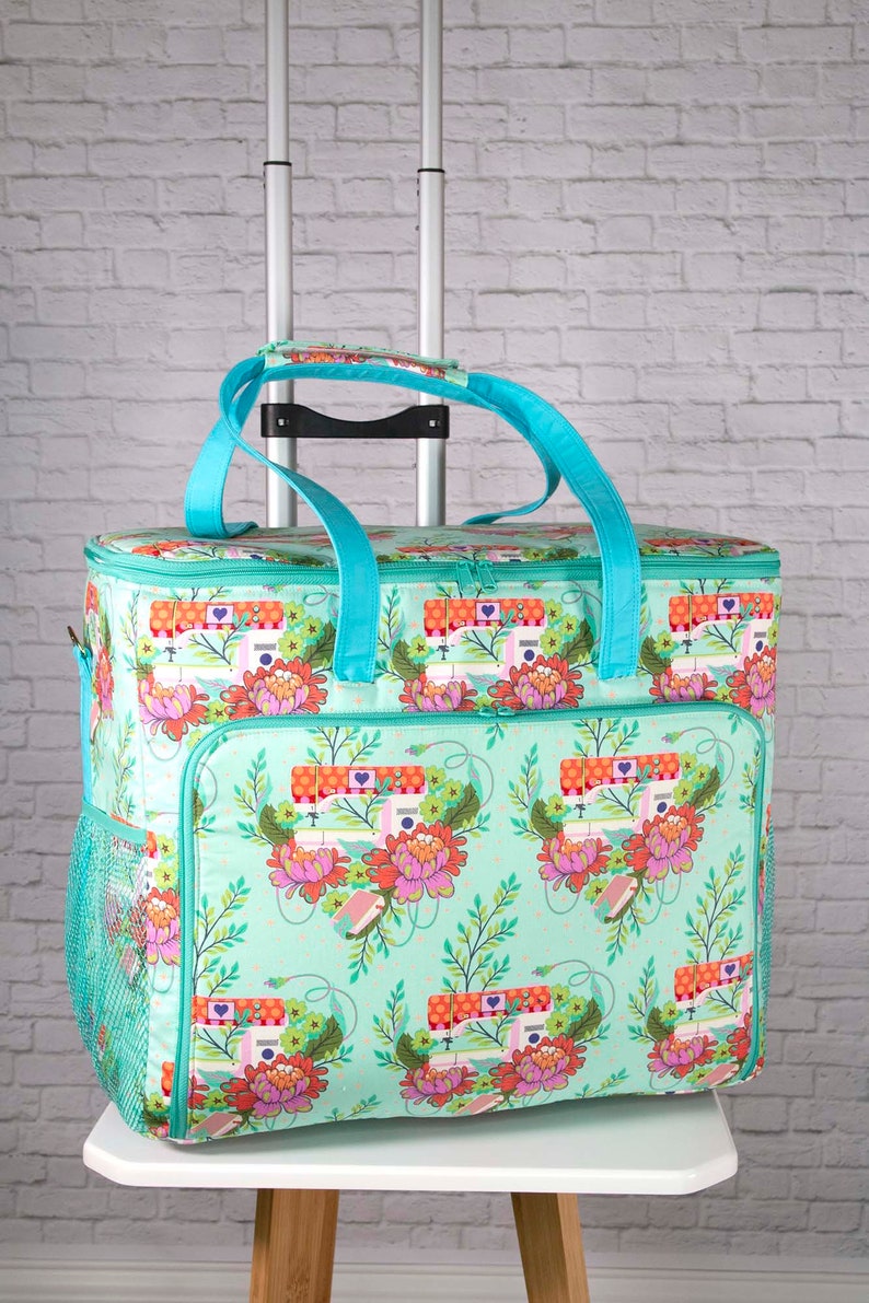 May include: A rolling sewing machine tote bag with a teal floral pattern featuring sewing machines and flowers. The bag has teal handles and trim, a mesh side pocket, and a telescoping handle for easy transport.