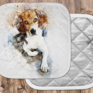 May include: A watercolor painting of a beagle dog with brown and white fur. The dog is sitting on a white background with splashes of orange and brown paint. The image is printed on a white pot holder with a quilted gray back.