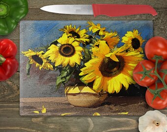 May include: A glass cutting board with a colorful illustration of sunflowers in a vase. The sunflowers are yellow with brown centers and green leaves. The vase is brown and has a textured surface. The background is a blue and gray watercolor wash.
