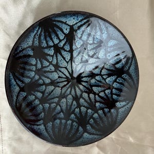 May include: Round ceramic plate with a dark blue and black floral pattern. The plate has a glossy finish and a slightly raised edge. The design features a network of dark lines against a lighter blue background.