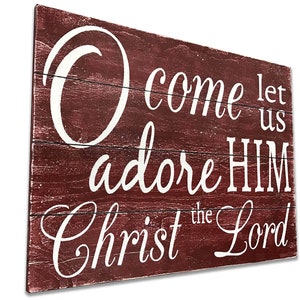 May include: A rustic wooden sign with a red background and white lettering. The sign reads "Come let us adore HIM Christ the Lord".