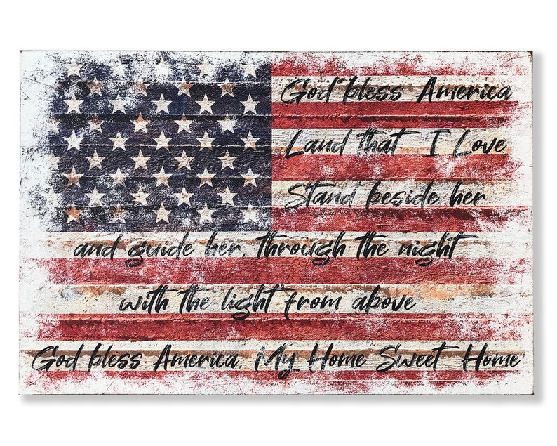 May include: A distressed wood sign with a faded American flag design and the text "God Bless America Land That I Love Stand Beside Her And Guide Her Through The Night With The Light From Above God Bless America My Home Sweet Home".