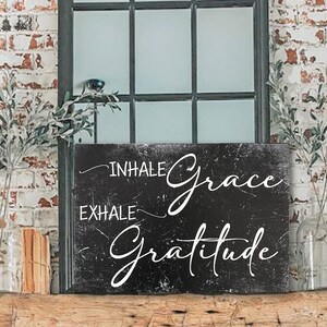 May include: Black and white sign with the text "Inhale Grace Exhale Gratitude" on a distressed background.