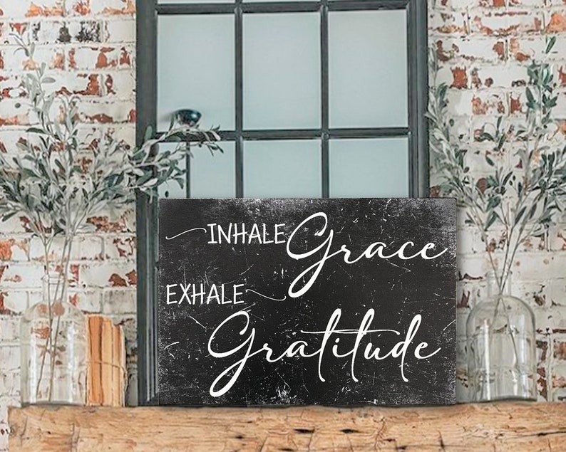 May include: Black and white sign with the text "Inhale Grace Exhale Gratitude" on a distressed background.