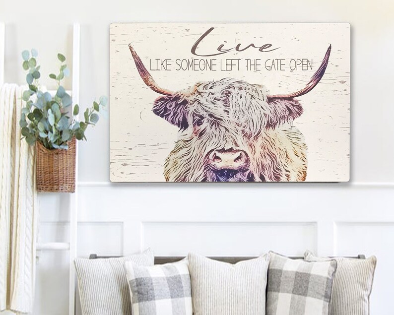 Op de afbeelding: Een rechthoekig houten bord met een illustratie van een Schotse Hooglander en de tekst "Live Like Someone Left The Gate Open". De koe heeft lang, ruig haar en grote hoorns. De achtergrond is licht, verweerd hout.