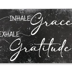 May include: Black and white sign with a distressed, chalkboard-like texture. The sign reads "INHALE grace EXHALE gratitude" in a white, cursive font.