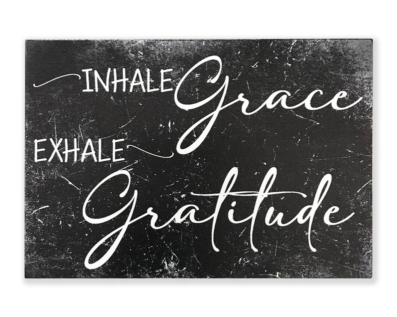 May include: Black and white sign with a distressed, chalkboard-like texture. The sign reads "INHALE grace EXHALE gratitude" in a white, cursive font.