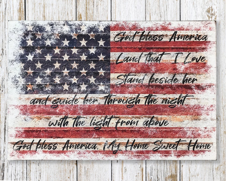 May include: A distressed wood sign with a faded American flag design and the lyrics to the patriotic song "God Bless America". The text reads: "God Bless America, Land That I Love, Stand Beside Her, And Guide Her Through The Night With The Light From Above, God Bless America, My Home Sweet Home."