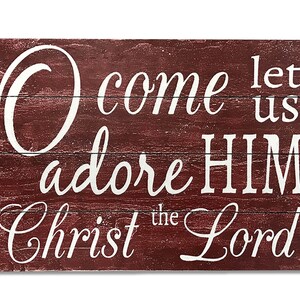 May include: A rustic wooden sign with a red background and white lettering. The sign reads "O come let us adore HIM Christ the Lord".