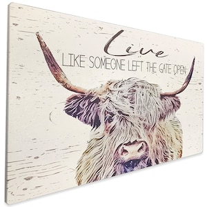 Op de afbeelding: Een rechthoekige wandkunstprint met een Schotse Hooglander met lange hoorns en ruige vacht. Het kunstwerk heeft een verweerde, vintage uitstraling met de woorden "Live Like Someone Left The Gate Open" in een scriptlettertype.