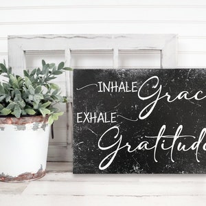 May include: Black and white sign with the text "INHALE grace EXHALE gratitude" in a distressed, handwritten font.