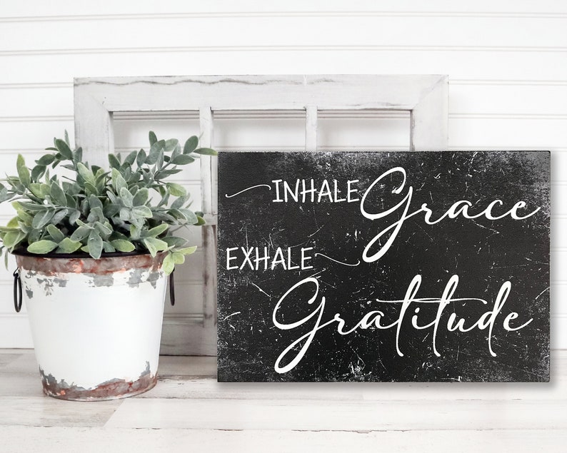 May include: Black and white sign with the text "INHALE grace EXHALE gratitude" in a distressed, handwritten font.