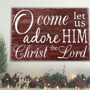 May include: Red wooden sign with white lettering that reads "O come let us adore HIM Christ the Lord".