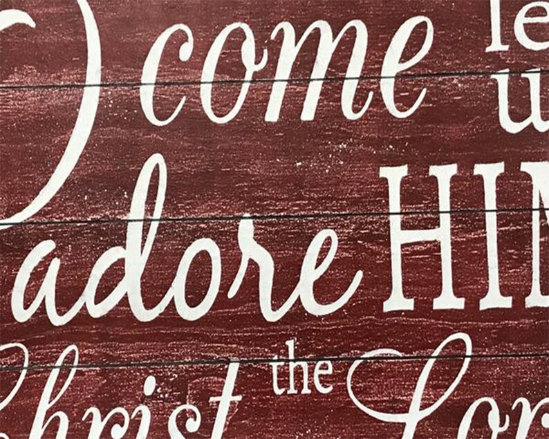 May include: Red wooden sign with white lettering that reads "O come let us adore Him, Christ the Lord".