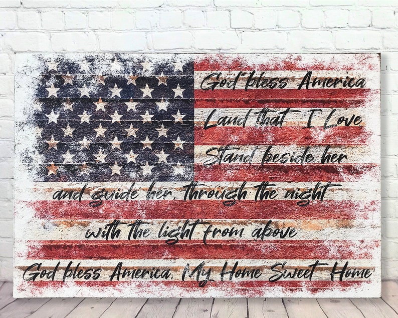 May include: A distressed wood sign with a faded American flag design and the lyrics to the patriotic song "God Bless America". The text reads "God bless America, Land that I love, Stand beside her, and guide her through the night with the light from above, God bless America, My Home Sweet Home."