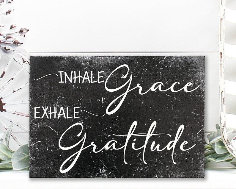 May include: Black and white sign with the text "Inhale Grace Exhale Gratitude" written in a cursive font. The sign has a distressed, vintage look.