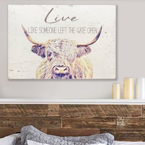 Op de afbeelding: Een rustiek houten wandkunstwerk met een illustratie van een Schotse Hooglander. De tekst "Live Like Someone Left The Gate Open" staat in grijs. De koe is afgebeeld in bruin- en beigetinten, wat een rustieke, vintage uitstraling geeft.