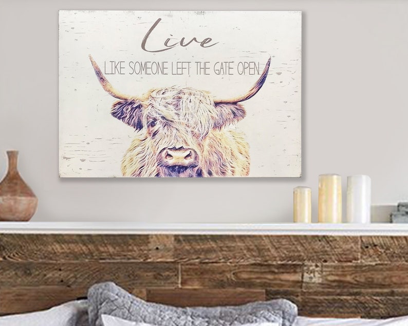 Op de afbeelding: Een rustiek houten wandkunstwerk met een illustratie van een Schotse Hooglander. De tekst "Live Like Someone Left The Gate Open" staat in grijs. De koe is afgebeeld in bruin- en beigetinten, wat een rustieke, vintage uitstraling geeft.