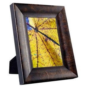 May include: A dark brown wood picture frame with a yellow leaf with black spots inside. The frame has a black stand.