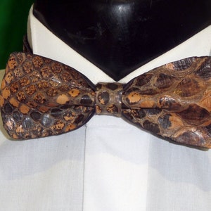 Op de afbeelding: Een bruine en beige leren strik met een slangenhuidpatroon.