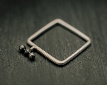 dunne vierkante zilveren ring; reliëf patroon bestaande uit drie kleine zwartgebarte zilveren knikkers