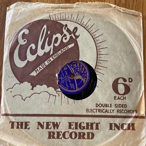 Op de afbeelding: Vintage Eclipse-plaat in een papieren hoes. De hoes is bruin met bruine tekst en een bruin Eclipse-logo. De plaat is zwart met een blauw en goudkleurig label. De hoes leest "The New Eight Inch Record".