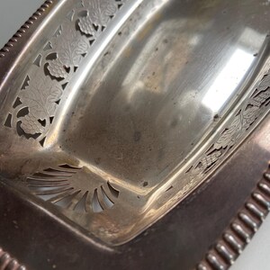 Può includere: Un vassoio da portata rettangolare argentato con decorativi motivi a intaglio di foglie d'uva e viti lungo i bordi. Il vassoio ha un bordo perlato e una superficie leggermente appannata, che mostra segni di età.