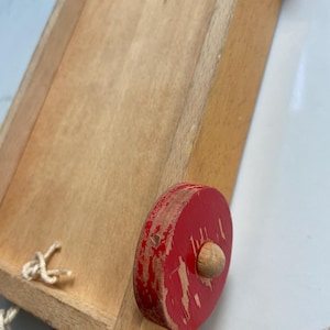 Può includere: Carriola giocattolo in legno con finitura in legno naturale e ruote rosse. La carriola ha un design semplice con una corda per tirare. Le ruote rosse mostrano segni di usura, aggiungendo fascino vintage.
