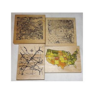 May include: Four wooden blocks with map designs. One block features a map of the United States with yellow, orange, and green coloring. Other blocks have vintage map illustrations of the world and a road map.