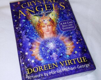 May include: A rectangular box set of Crystal Angels Oracle Cards by Doreen Virtue with artwork by Marius Michael-George. The cover features a winged figure holding a glowing blue crystal sphere against a deep blue background with stars.