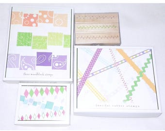 May include: Four boxes of rubber stamps with different designs. The boxes are white with colorful designs on the front. The text on the boxes reads "three woodblock stamps" and "fanciful rubber stamps".