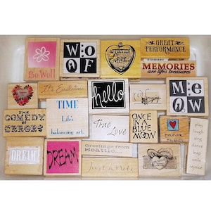 May include: A collection of wooden stamps with various phrases and designs. The stamps include words like "Hello", "Dream", and "Forever Friends", along with floral and heart motifs. The stamps are in various sizes and fonts.