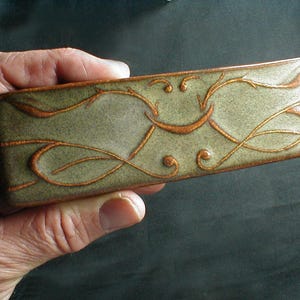 May include: A rectangular ceramic dish with a green glaze and a brown floral design. The dish is decorated with a swirling pattern of leaves and vines.