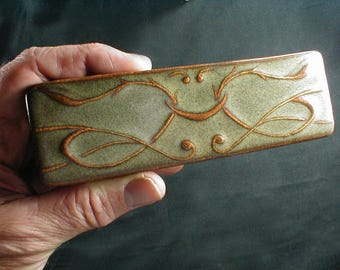 May include: A rectangular ceramic dish with a green glaze and a brown floral design. The dish is decorated with a swirling pattern of leaves and vines.