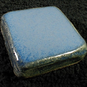 May include: A small, rectangular ceramic box with a light blue speckled lid and dark blue sides. The edges have a darker blue and green trim. The box is likely handmade and has a glossy finish. The box is a decorative item.